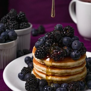 Stack of fluffy pancakes topped with fresh blackberries and blueberries, drizzled with honey, perfect for a delicious breakfast.