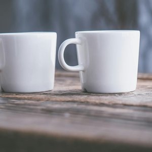 Close-up of two white ceramic cups on a rustic wooden table, featuring soft natural light.