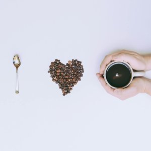 Coffee beans arranged in a heart shape with a mug and spoon on a white background.