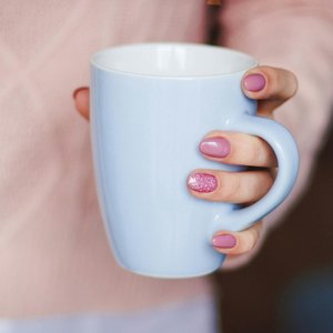 A woman's hand with pink nails holding a light blue mug, indoors.